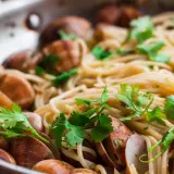 Spaghetti alle vongole surgelate, un piatto gustoso con pasta, cozze e prezzemolo fresco in una padella.