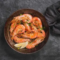 Gamberi in padella, succulenti e profumati, pronti per essere gustati con spicchi di limone fresco e un tocco di peperoncino.