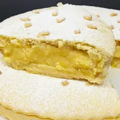 Torta vegana con crema gialla, ricoperta di zucchero a velo e pinoli. Un dolce delizioso e invitante.