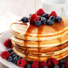 Pancakes con farina di avena, guarniti con frutti di bosco freschi e sciroppo d'acero che cola.