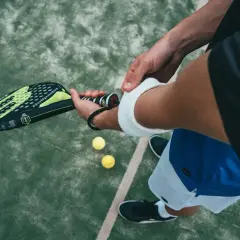 Giocatore di padel controlla la misura impugnatura racchetta padel, pronto per il servizio. Due palline gialle a terra.