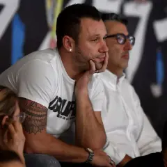 Antonio Cassano, con il suo tatuaggio distintivo, osserva concentrato un match di padel, immerso nell'atmosfera sportiva.