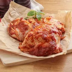 Cosce di pollo pronte per la marinatura, con pomodorini e peperoncino sullo sfondo.