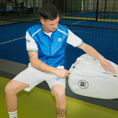Un giocatore di padel con abbigliamento sportivo bianco e blu, pronto per giocare. Scopri come vestirsi per giocare a padel con stile e comfort.
