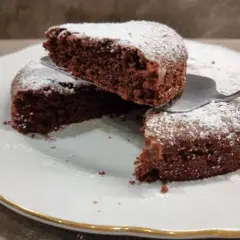 Una fetta di torta all'acqua al cacao, soffice e spolverata di zucchero a velo, viene sollevata da una paletta.