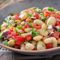 Insalata di fagioli bianchi, pomodori, cipolla rossa e erbe fresche in una ciotola rustica. Un piatto colorato e saporito.