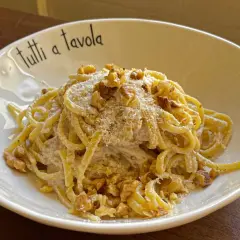 Pasta cremosa con pesto di noci, guarnita con noci tritate e parmigiano grattugiato. Un piatto invitante per tutti a tavola.