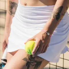 Braccialetto con ciondolo racchetta da padel, tatuaggio farfalla e rosa, palla da padel in mano.