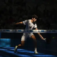 Arturo Coello in azione, colpisce la palla con la racchetta da padel, concentrato sul campo blu illuminato.