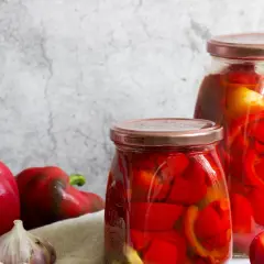 Barattoli di peperoni in agrodolce, con peperoni freschi e aglio sul lato.