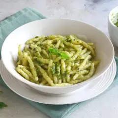 Un piatto di pasta al pesto fresco, con basilico e pinoli sparsi, pronto per essere gustato.