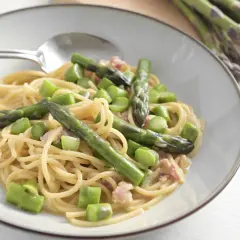 Un piatto di spaghetti con asparagi freschi e cubetti di speck croccante, condito con una cremosa salsa.