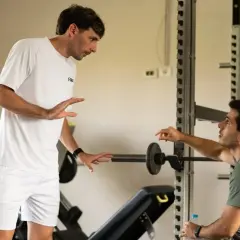 Due uomini discutono in palestra, uno in bianco, l'altro con maglia "bergamini padel".