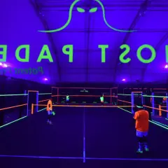 Campo da padel al neon con logo "Ghost Padel" e giocatori in azione.