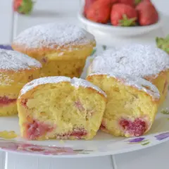 Morbidi muffin alle fragole, cosparsi di zucchero a velo, su un piatto fiorito. Uno è tagliato a metà, rivelando il ripieno succoso.