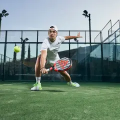 Ale Galán in azione, con le sue scarpe da padel che spiccano sul campo verde. Colpisce la palla con determinazione.