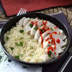 Delizioso pollo in padella a fette, servito su couscous e guarnito con salsa piccante e coriandolo fresco.