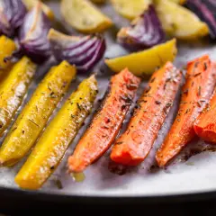 Carote gialle e arancioni, cipolle rosse e patate dorate, condite con erbe aromatiche, pronte per essere gustate come deliziose verdure miste al forno.