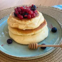 Pancake ricetta: soffici pancake impilati, guarniti con frutti di bosco e miele, pronti per essere gustati.