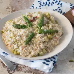 Un cremoso risotto con asparagi e pancetta, guarnito con punte di asparagi freschi e una spolverata di parmigiano.