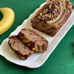 Delizioso banana bread light con gocce di cioccolato e noci, guarnito con banana e servito su un piatto bianco.