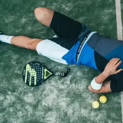 Giocatore di padel esausto, con racchetta e palline accanto. Forse ha appena eseguito un potente head smash.