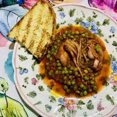 Piatto di totani con piselli in umido, accompagnato da una fetta di pane abbrustolito, su un piatto decorato con fiori e uccelli.