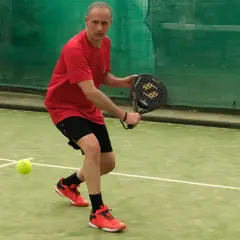 Uomo in campo da padel, pronto a colpire la palla. Un momento di gioco intenso nel padel Italia.