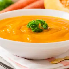 Una cremosa vellutata di carote, guarnita con prezzemolo fresco, pronta per essere gustata.
