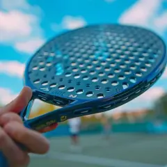 Racchette padel controllo: impugnatura blu di una racchetta da padel con campo e cielo sullo sfondo.