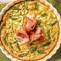 Frittata di asparagi al forno, dorata e invitante, guarnita con fette di prosciutto crudo. Un piatto perfetto per un pranzo leggero.