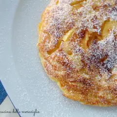 Frittata di mele in padella pronta in 5 minuti, cosparsa di zucchero a velo, su un piatto bianco accanto a una tovaglia a quadri blu.
