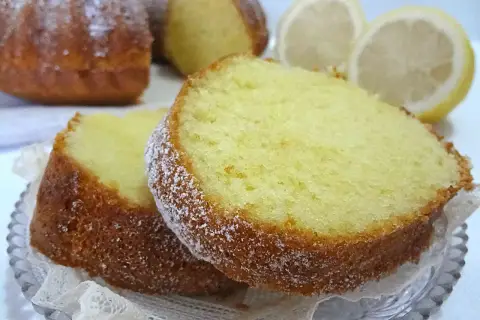 Fette di ciambellone al limone spolverate di zucchero a velo, con spicchi di limone sullo sfondo.