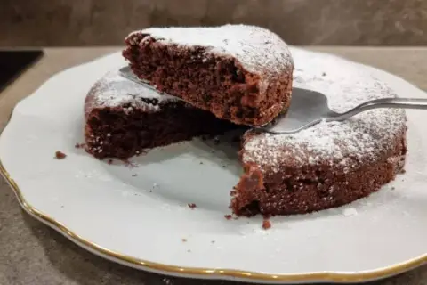 Una fetta di torta all'acqua al cacao, soffice e spolverata di zucchero a velo, viene sollevata da una paletta.