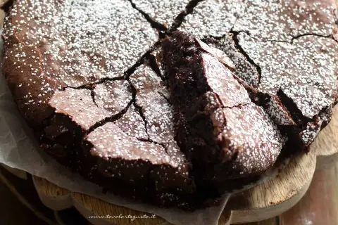 Torta al cioccolato fondente, con una crosta screpolata e cosparsa di zucchero a velo, pronta per essere gustata.
