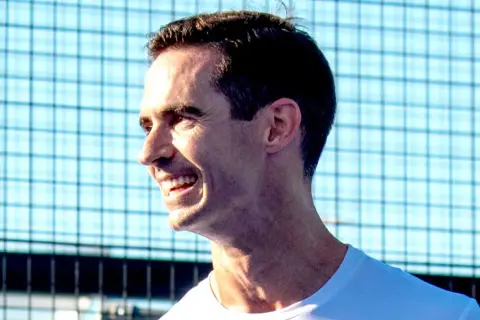 Un uomo sorride con entusiasmo, pronto per una partita di padel.