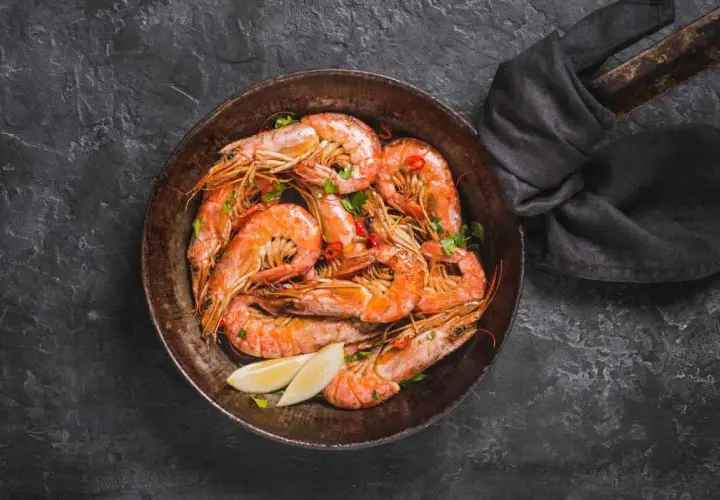 Gamberi in padella, succulenti e profumati, pronti per essere gustati con spicchi di limone fresco e un tocco di peperoncino.