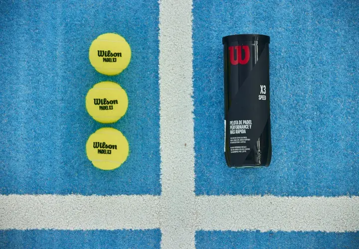 Tre palline da padel Wilson X3 e un tubetto, pronte per una partita veloce sul campo blu.