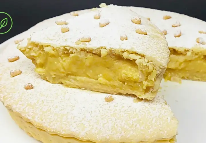 Torta vegana con crema gialla, ricoperta di zucchero a velo e pinoli. Un dolce delizioso e invitante.