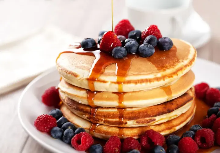 Pancakes con farina di avena, guarniti con frutti di bosco freschi e sciroppo d'acero che cola.