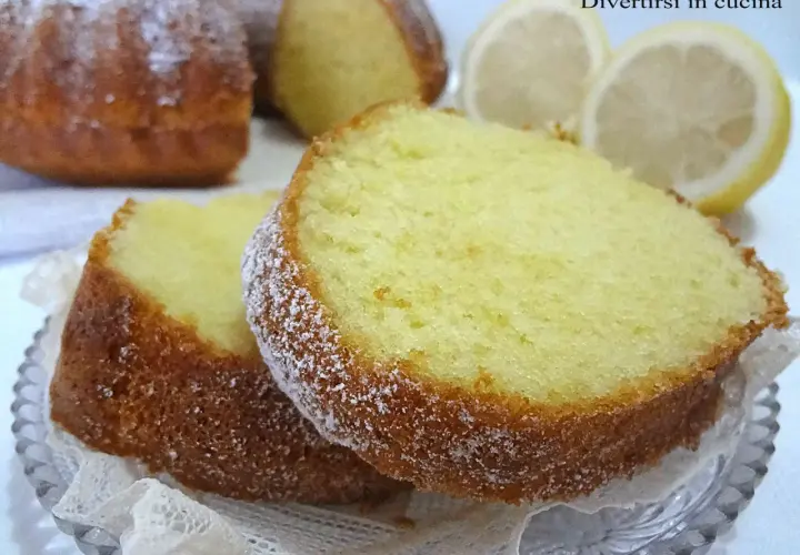 Fette di ciambellone al limone spolverate di zucchero a velo, con spicchi di limone sullo sfondo.