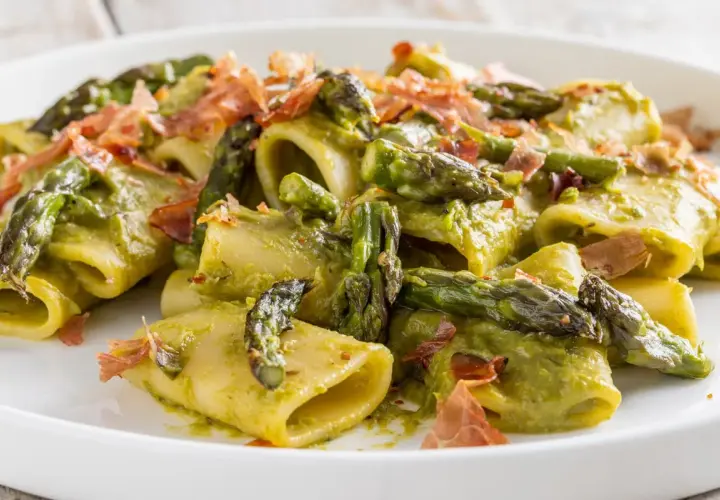 Paccheri conditi con una cremosa salsa verde e asparagi selvatici croccanti, guarniti con scaglie di prosciutto.