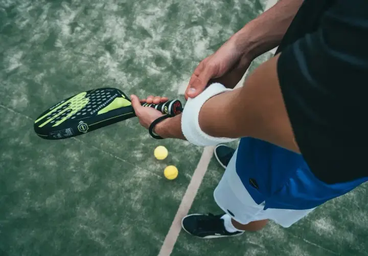 Giocatore di padel controlla la misura impugnatura racchetta padel, pronto per il servizio. Due palline gialle a terra.