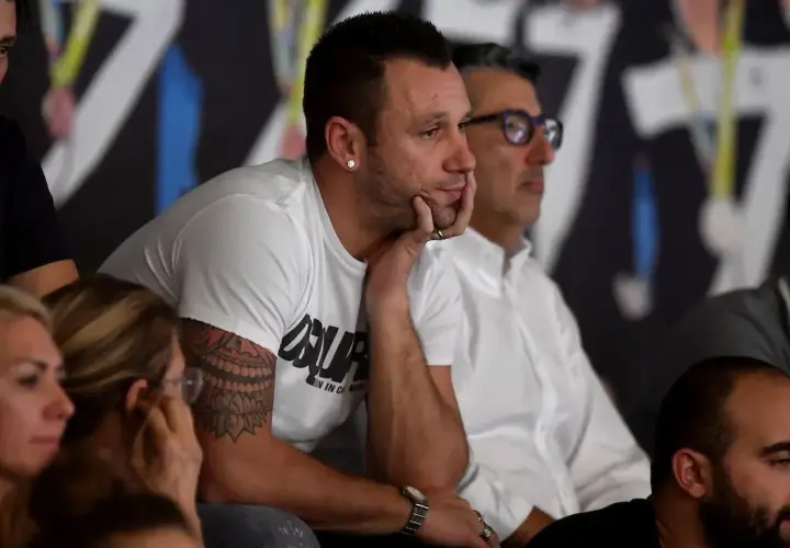 Antonio Cassano, con il suo tatuaggio distintivo, osserva concentrato un match di padel, immerso nell'atmosfera sportiva.
