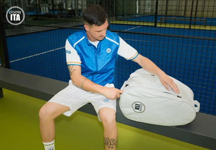 Un giocatore di padel con abbigliamento sportivo bianco e blu, pronto per giocare. Scopri come vestirsi per giocare a padel con stile e comfort.