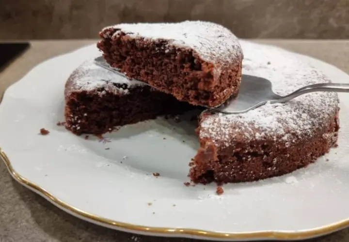 Una fetta di torta all'acqua al cacao, soffice e spolverata di zucchero a velo, viene sollevata da una paletta.