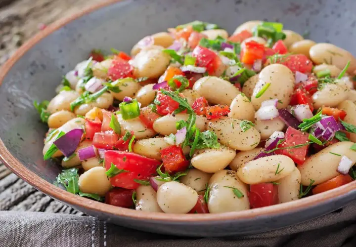 Insalata di fagioli bianchi, pomodori, cipolla rossa e erbe fresche in una ciotola rustica. Un piatto colorato e saporito.