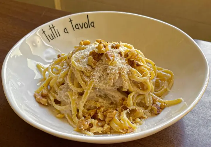 Pasta cremosa con pesto di noci, guarnita con noci tritate e parmigiano grattugiato. Un piatto invitante per tutti a tavola.