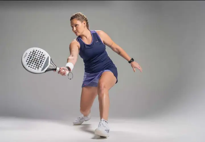 Giocatrice di padel in azione, con racchetta in mano, pronta a colpire la palla. La sua concentrazione è palpabile, un vero esempio di passione per il **padel**.