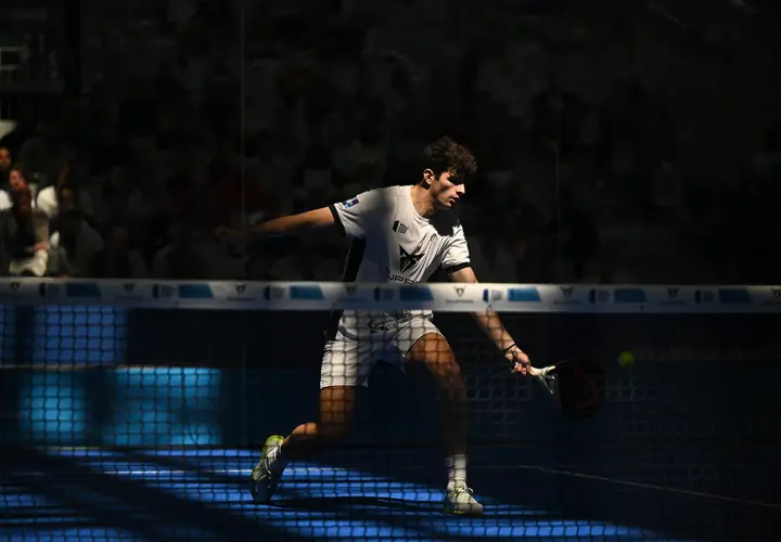 Arturo Coello in azione, colpisce la palla con la racchetta da padel, concentrato sul campo blu illuminato.